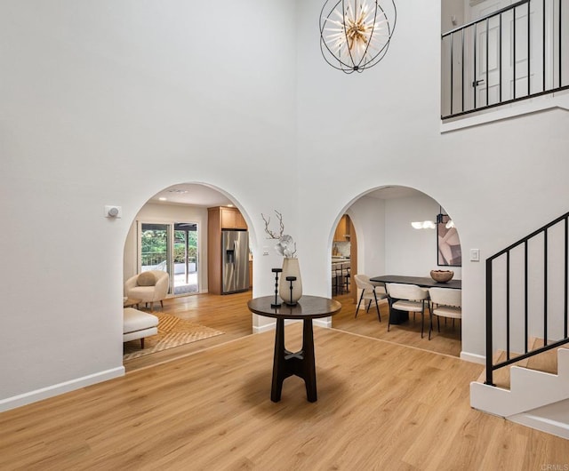 foyer entrance featuring light wood-type flooring, arched walkways, a chandelier, and stairway