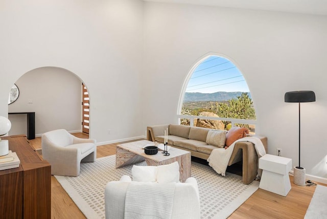 living area with a mountain view, arched walkways, a high ceiling, and light wood-style flooring