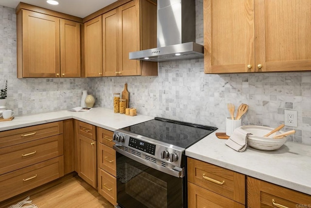 kitchen with light wood finished floors, light countertops, stainless steel range with electric stovetop, wall chimney exhaust hood, and tasteful backsplash