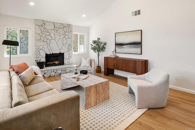 living room with wood finished floors, a fireplace, visible vents, and lofted ceiling