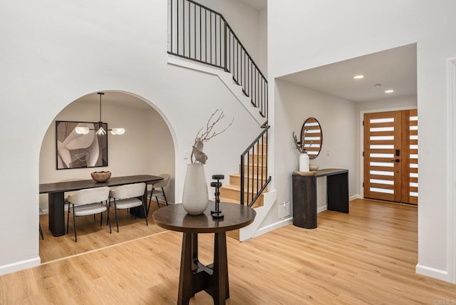 foyer featuring arched walkways, a high ceiling, light wood finished floors, baseboards, and stairs