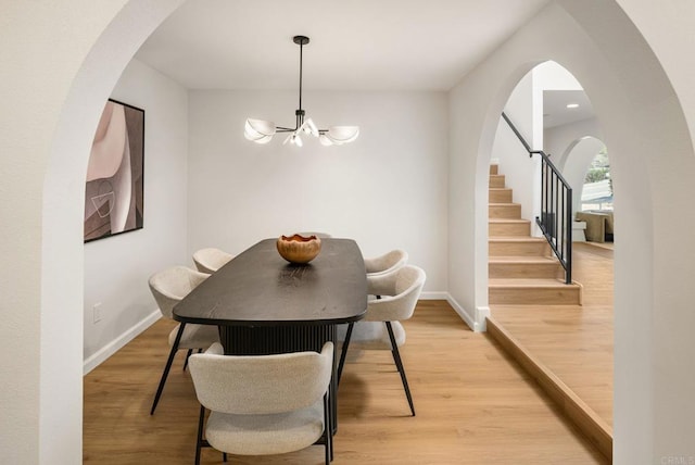 dining room featuring a notable chandelier, light wood-style flooring, arched walkways, baseboards, and stairs