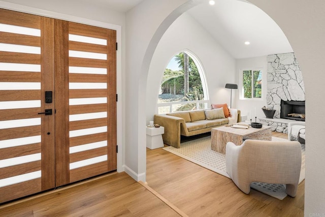 living area with light wood finished floors, vaulted ceiling, recessed lighting, a fireplace, and arched walkways