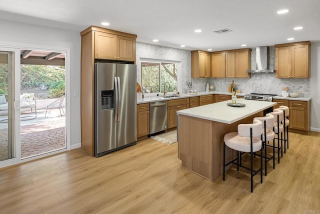 kitchen with visible vents, wall chimney range hood, stainless steel appliances, a breakfast bar area, and light wood finished floors