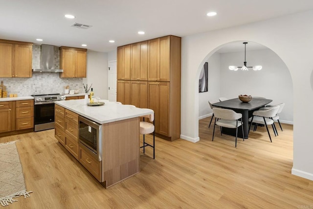 kitchen featuring visible vents, a breakfast bar, arched walkways, appliances with stainless steel finishes, and wall chimney range hood