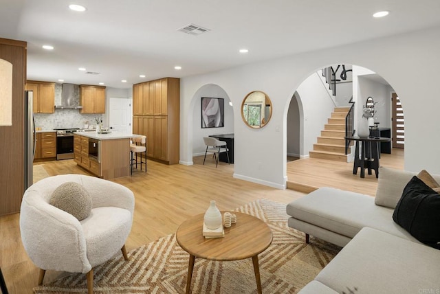 living room featuring stairway, visible vents, recessed lighting, arched walkways, and light wood-type flooring