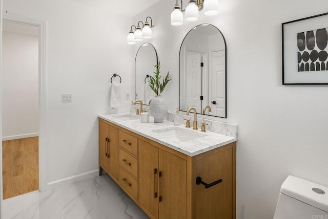 full bath with double vanity, baseboards, marble finish floor, and a sink