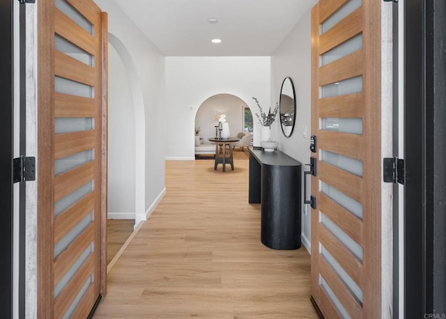 hall with recessed lighting, baseboards, arched walkways, and light wood-style flooring