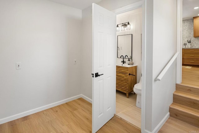 hallway with stairway, baseboards, light wood-type flooring, and a sink