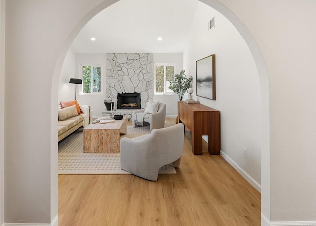 living area with visible vents, arched walkways, light wood-style floors, a fireplace, and baseboards