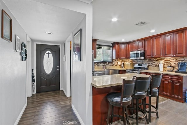 kitchen featuring wood finished floors, visible vents, decorative backsplash, dark brown cabinets, and appliances with stainless steel finishes