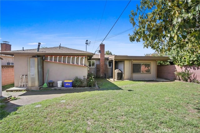 back of house with stucco siding, a yard, a chimney, and fence