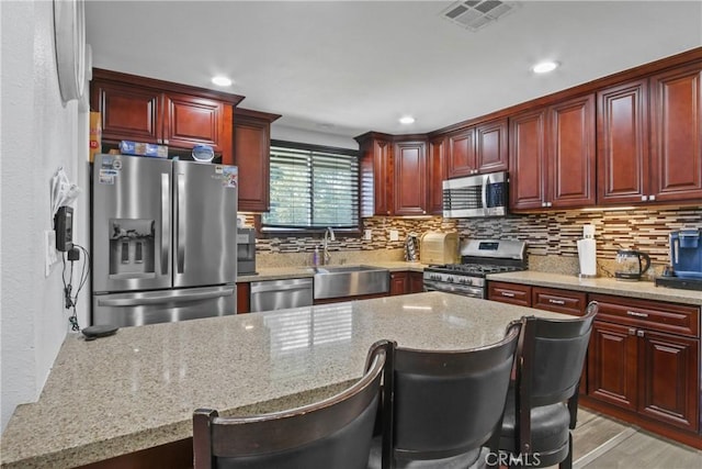 kitchen featuring visible vents, a sink, reddish brown cabinets, appliances with stainless steel finishes, and light stone countertops