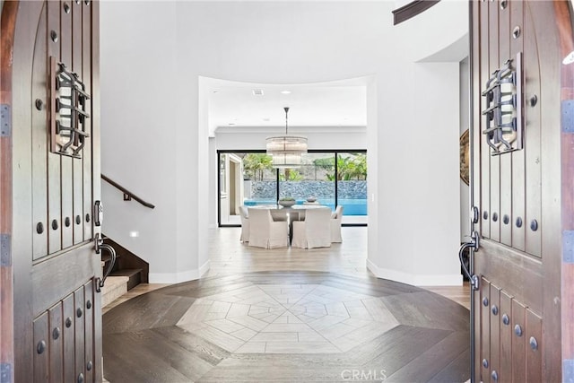 entryway featuring baseboards, a notable chandelier, and stairs