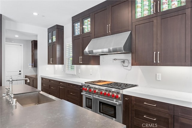 kitchen with under cabinet range hood, double oven range, dark brown cabinets, and a sink