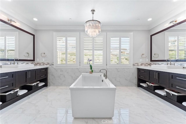 full bath with marble finish floor, a freestanding bath, two vanities, and a sink