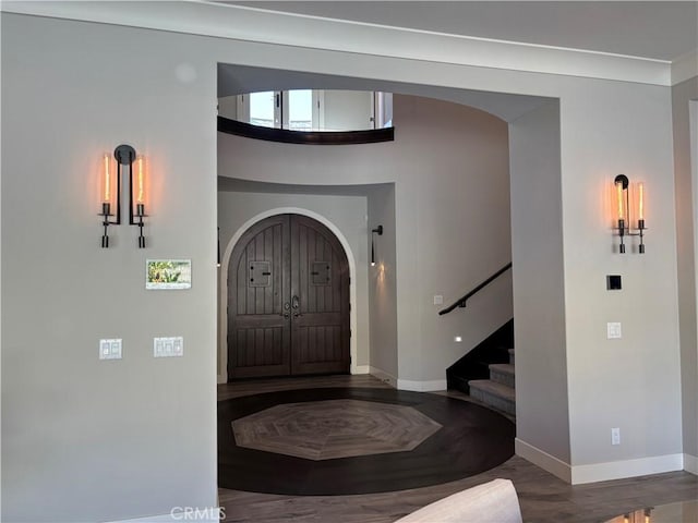 foyer entrance featuring baseboards, arched walkways, and stairway