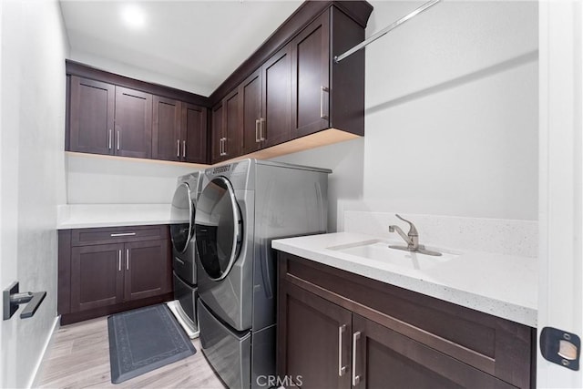 laundry room featuring light wood finished floors, a sink, cabinet space, and separate washer and dryer