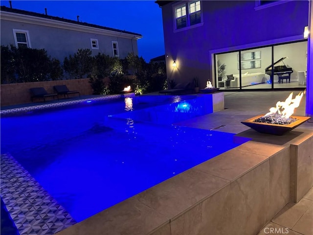 pool at night with a patio, a fenced in pool, and an outdoor fire pit