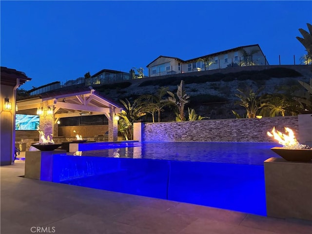 pool at night featuring an outdoor pool and a fire pit