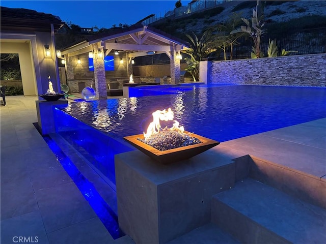 pool at night with a gazebo, a fenced in pool, and an outdoor fire pit