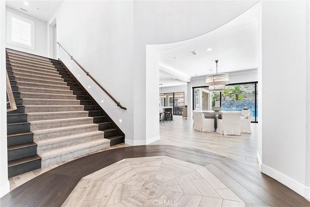 entrance foyer featuring a notable chandelier, stairway, baseboards, and a towering ceiling