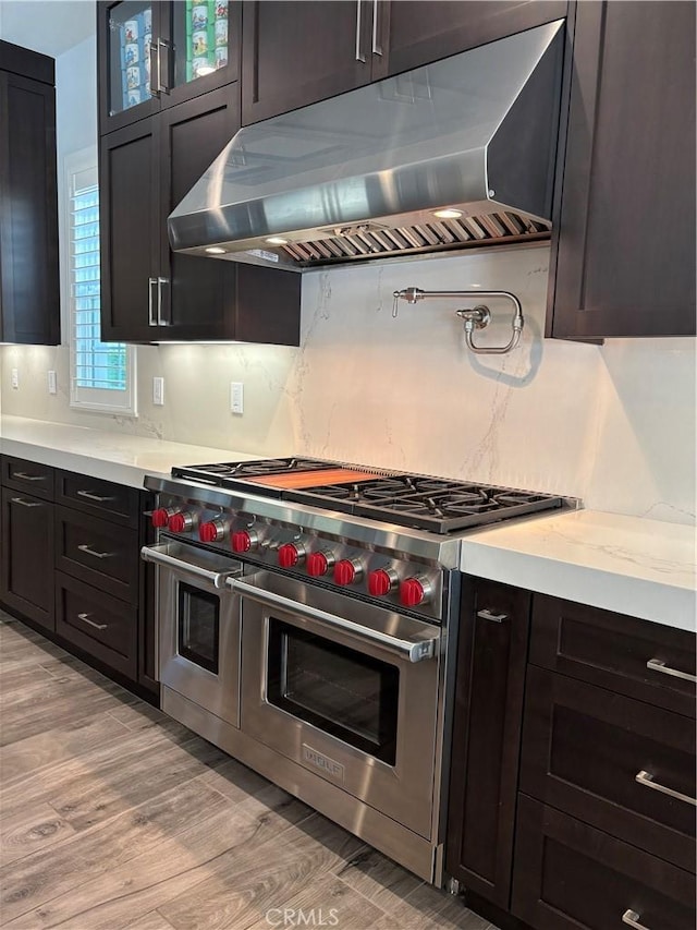 kitchen with glass insert cabinets, under cabinet range hood, double oven range, decorative backsplash, and light wood-style floors