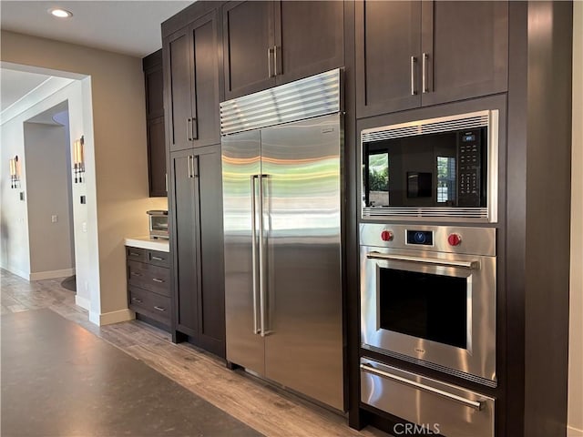 kitchen featuring a warming drawer, dark brown cabinets, light wood-style floors, and built in appliances