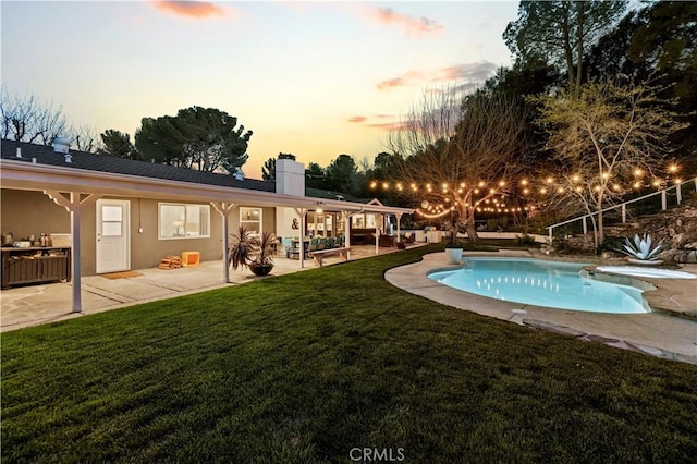 pool at dusk with an outdoor pool, a patio, and a lawn