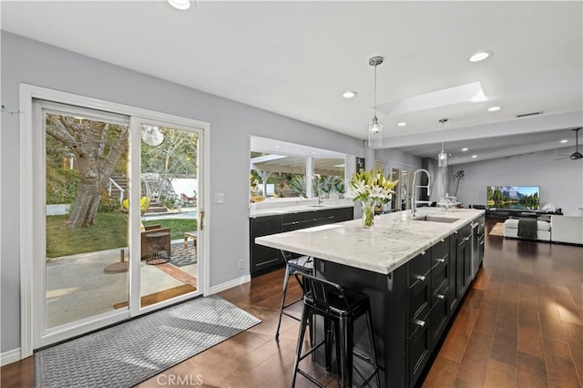 kitchen with a kitchen island with sink, a sink, open floor plan, dark cabinetry, and recessed lighting