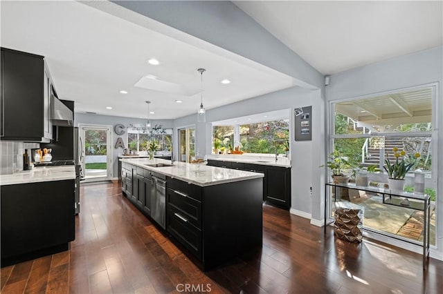 kitchen with backsplash, dark wood finished floors, a center island with sink, pendant lighting, and dark cabinets