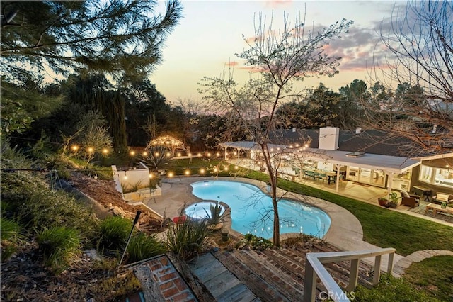 pool at dusk with an outdoor pool and a patio