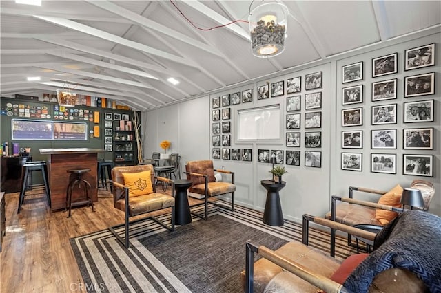 living area featuring a bar, lofted ceiling with beams, and wood finished floors