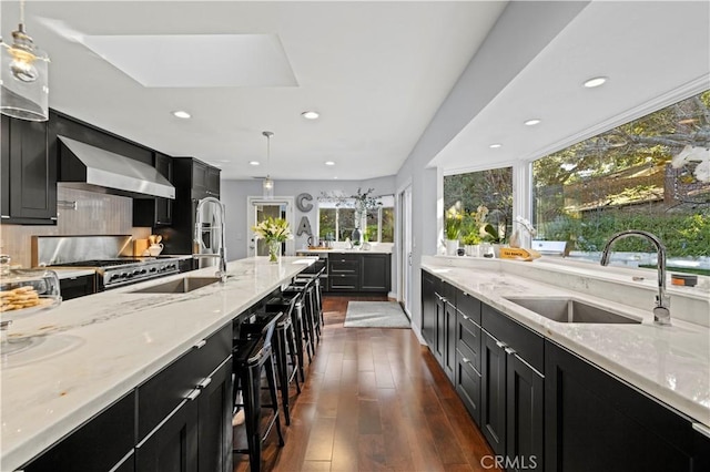 kitchen featuring stove, wall chimney exhaust hood, dark cabinets, and a sink