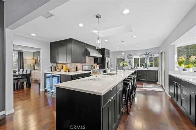 kitchen featuring light stone countertops, visible vents, a sink, wine cooler, and wall chimney exhaust hood