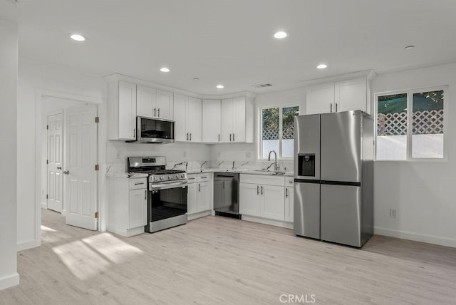 kitchen with light wood finished floors, backsplash, appliances with stainless steel finishes, white cabinets, and a sink