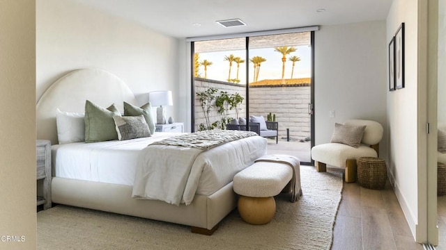 bedroom with access to outside, visible vents, a wall of windows, and wood finished floors