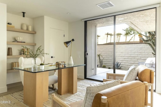 office with visible vents, light wood-type flooring, baseboards, and expansive windows