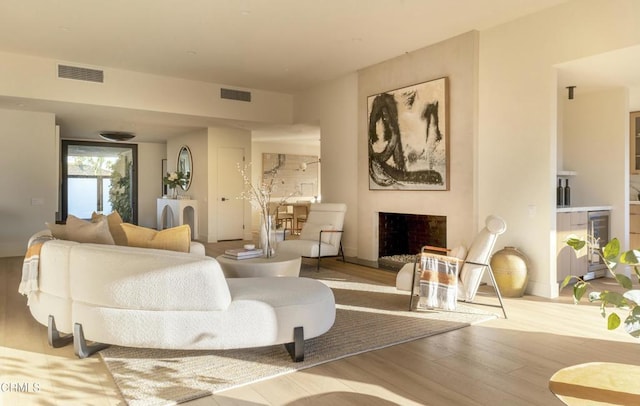 living area featuring beverage cooler, wood finished floors, a fireplace, and visible vents