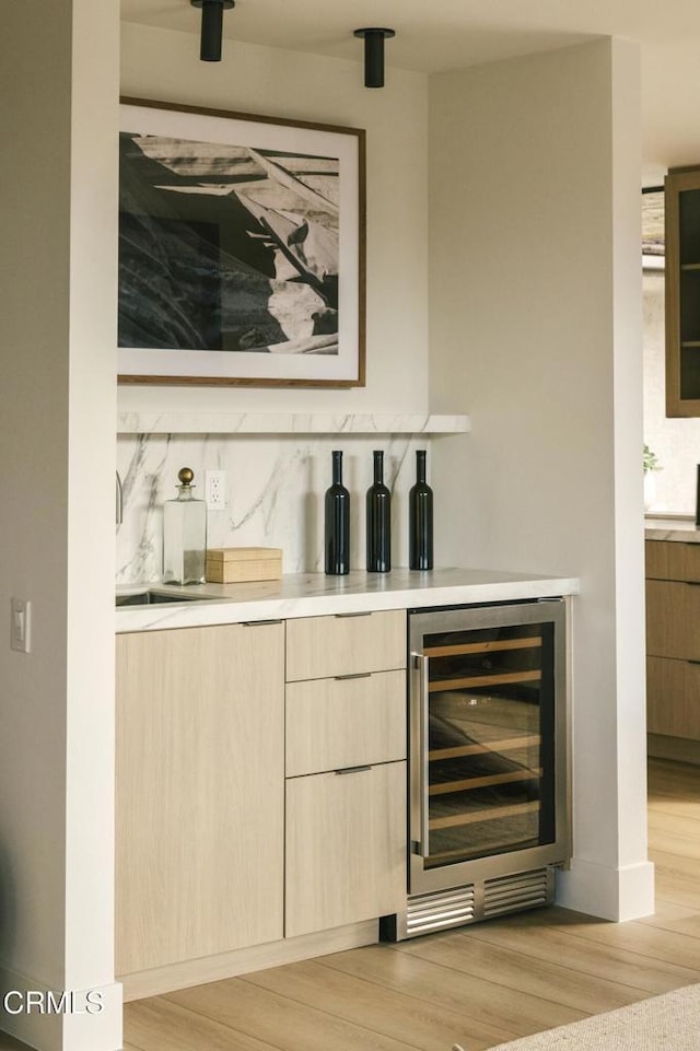 bar featuring wine cooler, light wood-style floors, backsplash, and a sink