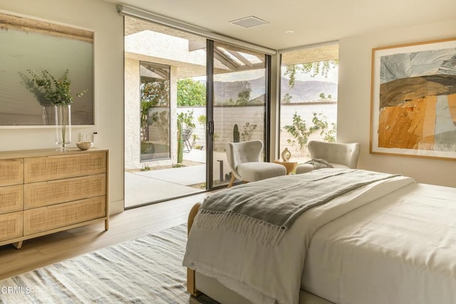 bedroom with wood finished floors, access to exterior, and floor to ceiling windows