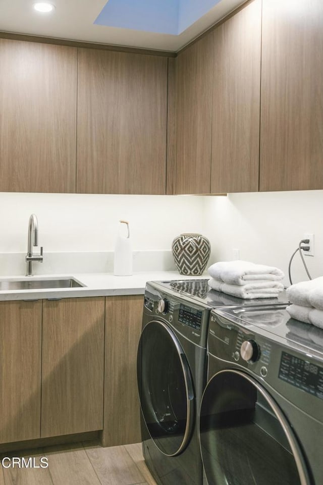 laundry area with washing machine and clothes dryer, cabinet space, light wood-style floors, and a sink