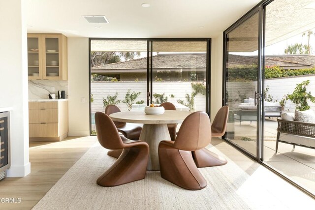 interior space featuring light wood-type flooring, visible vents, expansive windows, wine cooler, and baseboards