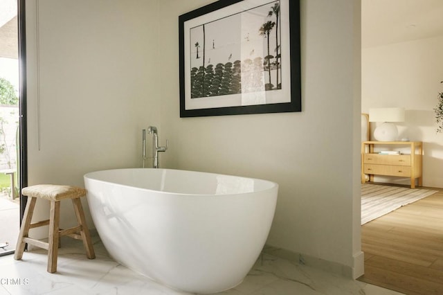 bathroom with baseboards, marble finish floor, and a freestanding bath