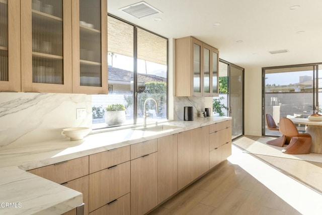 kitchen featuring light brown cabinetry, light stone countertops, light wood-type flooring, and a sink