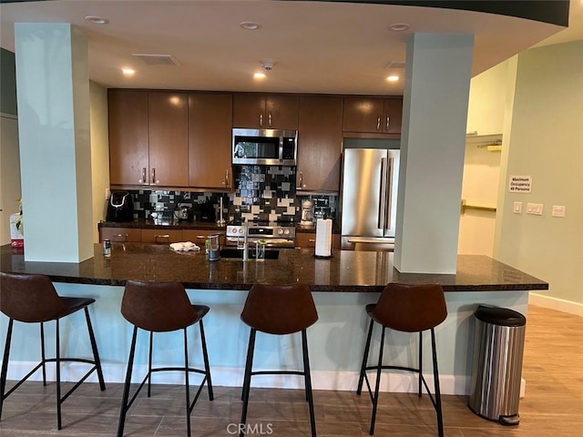 kitchen with light wood-style flooring, a sink, appliances with stainless steel finishes, a kitchen breakfast bar, and tasteful backsplash