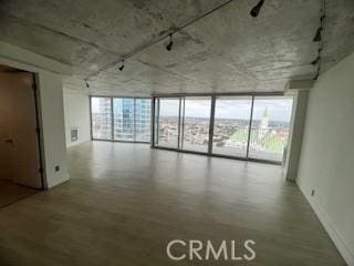 unfurnished room featuring floor to ceiling windows, wood finished floors, and baseboards