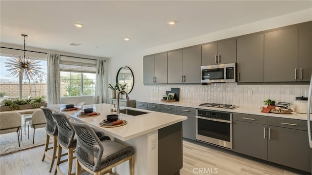 kitchen with backsplash, a breakfast bar, gray cabinets, appliances with stainless steel finishes, and a sink