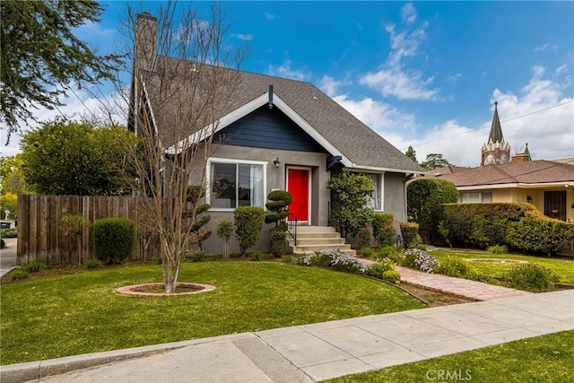 view of front facade featuring stucco siding, a shingled roof, a front lawn, and fence