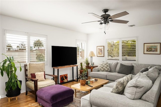 living room featuring ceiling fan, visible vents, baseboards, and wood finished floors